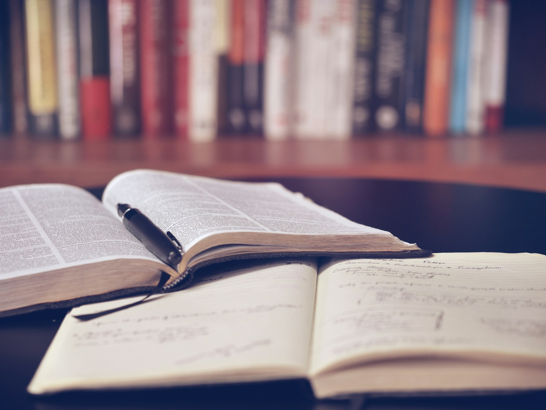 Libri aperti con una penna appoggiata tra le pagine, in luce calda, con profondità di campo ridotta