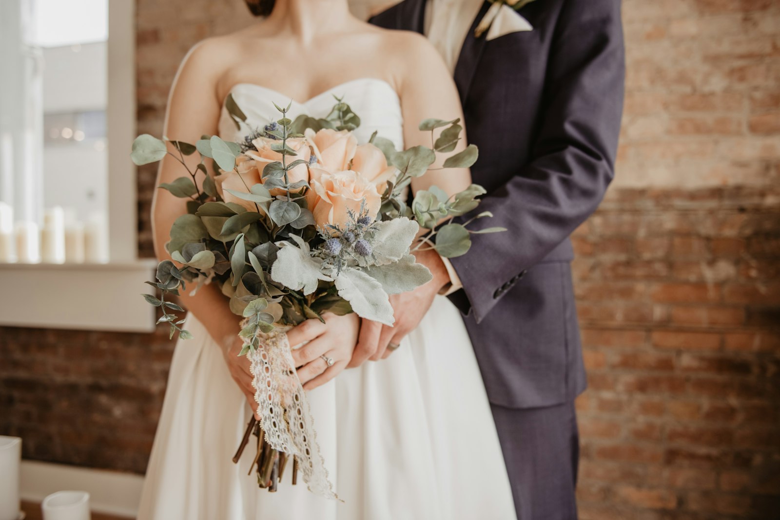 Una coppia di sposi tiene un bouquet davanti a un muro di mattoni