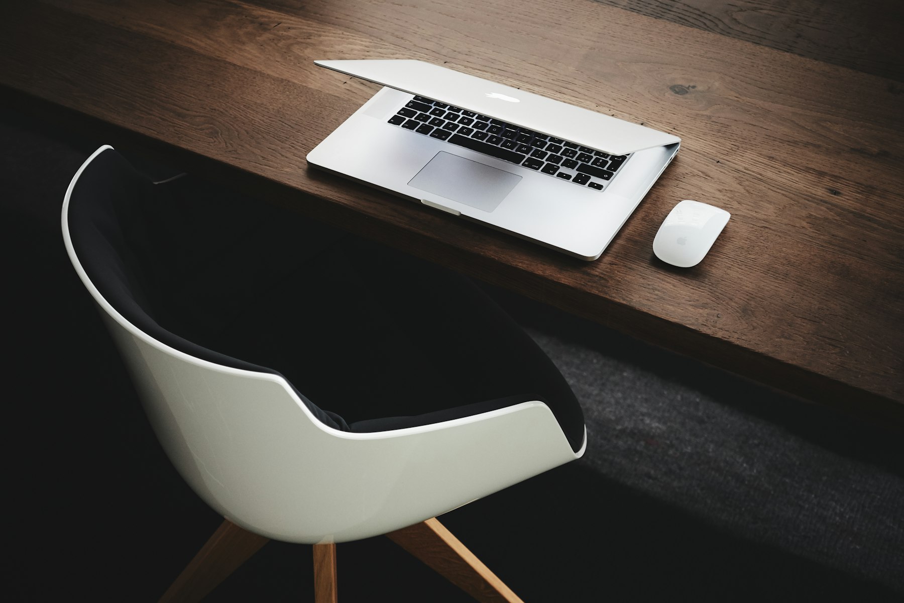 Una scrivania minimalista in legno scuro con un laptop e una sedia bianca