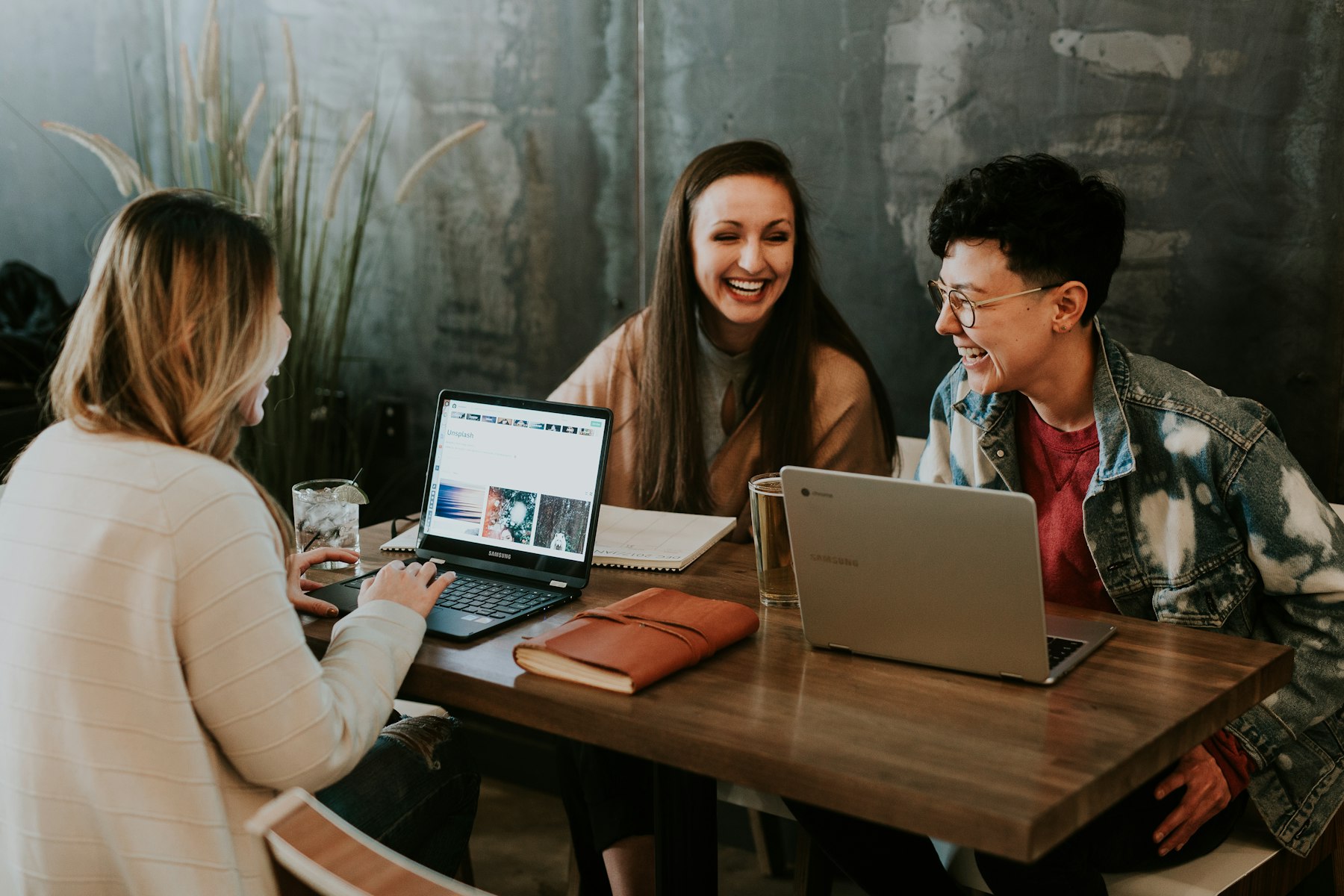 Drei Freunde lachen zusammen an einem Tisch mit Laptops