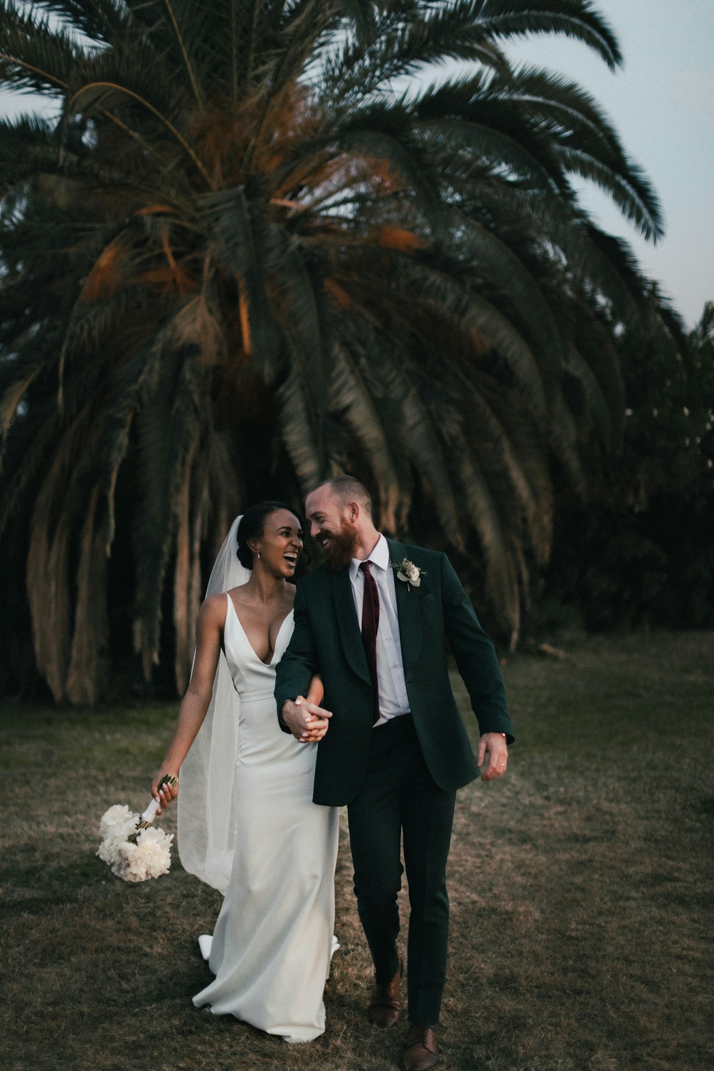 A couple walking at dusk under a large palm tree